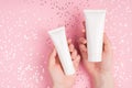 Close up photo of female woman hands holding two size tubes with mock up empty blank space over white shimmer pastel background Royalty Free Stock Photo