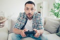 Close up photo of focused handsome mature guy hold hand have play station game pad dressed plaid denim jeans sit divan