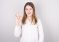 Close-up photo of funny young brunette woman in white shirt showing OK gesture  looking at camera  isolated on gray background Royalty Free Stock Photo