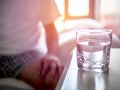 Close Up photo glass of water on bedside table man sitting in bed