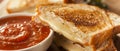 A close-up photo of a grilled cheese sandwich cut in half, revealing melted cheese and a bowl of tomato soup on a white Royalty Free Stock Photo