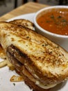 A close-up photo of a grilled cheese sandwich cut in half, revealing melted cheese and a bowl of tomato soup on a white Royalty Free Stock Photo