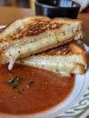 A close-up photo of a grilled cheese sandwich cut in half, revealing melted cheese and a bowl of tomato soup on a white Royalty Free Stock Photo