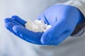 A close-up photo of a hand in a protective medical glove on which lies a handful of white pills