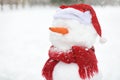 Close-up photo of a handmade snowman with a scarf, Santa Claus hat and carrot nose in a snowy park Royalty Free Stock Photo