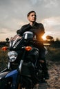 Close-up photo of handsome biker sitting on motorcycle in sunset on the country road. Royalty Free Stock Photo