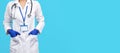 Close up photo of handsome young woman doctor with stethoscope, gloves and badge over blue background. Copy space. Royalty Free Stock Photo