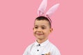 Close up photo of a little boy in white t-shirt wearin bunny earson head smiling and posing on pink background, Easter