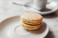Close up photo of macaron with salted caramel on a saucer with blurred cup of coffee on the background