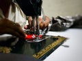 Close up photo of manual sewing machine with tailor hands stitching red cloth with selective focus