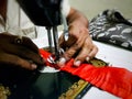 Close up photo of manual sewing machine with tailor hands stitching red cloth with selective focus