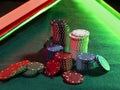 Close-up photo of a multicolored chips piles, some of them laying nearby on green cover of playing table, under green Royalty Free Stock Photo