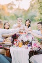 The close-up photo of the newlyweds and guests clinking their glasses and sitting at the table full of delicious food