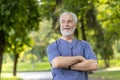 A close-up photo of an older gray-haired man standing in casual clothes in nature, crossing his arms on the ground and Royalty Free Stock Photo