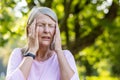 A close-up photo of an older gray-haired woman standing on the street in the park and holding her head with her hands Royalty Free Stock Photo