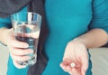 Close up photo of one round white pill in young female hand. Woman takes medicines with glass of water. Royalty Free Stock Photo