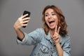 Close-up photo of overjoyed brunette teen girl showing peace gesture while making selfie on mobile phone Royalty Free Stock Photo