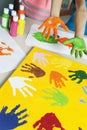Close-up of paint covered hands and colorful handprints on papers