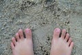 close up photo of a pair of small child& x27;s feet standing on the sand.