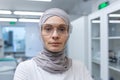 Close-up photo. Portrait of a young Muslim female lab assistant, pharmacist, scientist in hijab and protective glasses
