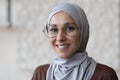 Close up photo portrait of young smiling Muslim woman in glasses and gray hijab, Arab woman at home smiling and looking Royalty Free Stock Photo