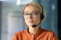 Close-up photo. Portrait of a young woman in a headset, glasses and an orange shirt looking at the camera Royalty Free Stock Photo