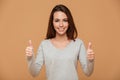 Close-up photo of pretty young woman in gray blouse showing thumb up gesture, looking at camera