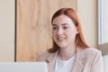 Close-up photo of a red haired business woman smiling while sitting at a computer, got a satisfactory result