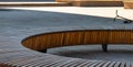 Close-up photo of a round wooden bench showing the color and arrangement of the wood and also the background of a scooter left on