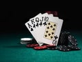 Royal flush standing leaning on colorful chips piles on green cover of playing table. Black background. Close-up. Royalty Free Stock Photo