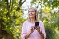 Close-up photo of a senior gray-haired woman doing sports and walking in the park, standing in headphones, holding a Royalty Free Stock Photo