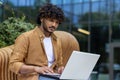 Close-up photo of a serious and focused Indian man sitting on a bench outside wearing headphones, working and studying Royalty Free Stock Photo