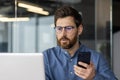 Close-up photo of a serious and focused man in glasses and a shirt working in the office on a laptop and holding a Royalty Free Stock Photo