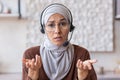 Close-up photo. Serious and frustrated young muslim woman in hijab and wearing headset and glasses talking and