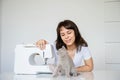 Photo of a sexy brunette working at the sewing machine and playing with a gray kitten Royalty Free Stock Photo