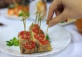 Close up photo with slelctive focus of female hand picking meat roll with tomato and sesame from white plate on table Royalty Free Stock Photo