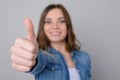 Close up photo of smiling happy cute woman in casual clothes showing thumb up. She is isolated on grey background good great deal