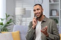 Close-up photo. Smiling hispanic young man sitting on the sofa at home and talking on the phone, gesturing with his Royalty Free Stock Photo