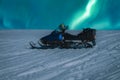 Close up photo on snow mobile standing at snow slope at night with with night northern green lights in starry sky. Norway, Sweden