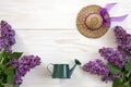 Close up photo with toy watering can, Little straw hat and lilac on white wooden background. Spring background, top view, close up