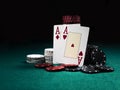 Two aces hearts and diamonds standing leaning on chips piles, some of them laying nearby on green cover of playing table