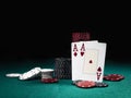 Two aces hearts and diamonds standing leaning on chips piles, some of them laying nearby on green cover of playing table