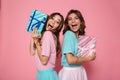 Close-up photo of two overjoyed female friends in colorful tshirts holding gift boxes, looking at camera