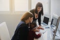 Photo of two women in office outfit working on computers and discussing a report on the floor; one of them is with a baby girl in Royalty Free Stock Photo