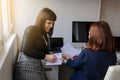 Photo of two women in office outfit working on computers and discussing a report on the floor; one of them is with a baby girl in Royalty Free Stock Photo