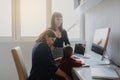 photo of two women in office outfit working on computers and discussing a report; one of them is with a baby girl in her arms