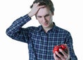 Close-up photo of upset young man with hand in hair holding red alarm clock, isolated over gray background. Royalty Free Stock Photo