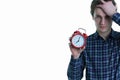 Close-up photo of upset young man with hand in hair holding red alarm clock, isolated over white background. Royalty Free Stock Photo