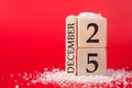 Close up photo of wooden cube calendar showing date of christmas isolated on red background with snow