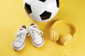 Close-up photo of yellow headphones, white sneakers and traditional style soccer ball over yellow background. Royalty Free Stock Photo